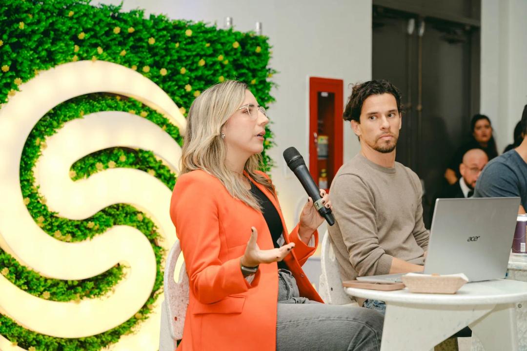 Mujer hablo por un micrófono mientras un hombre la mira atentamente