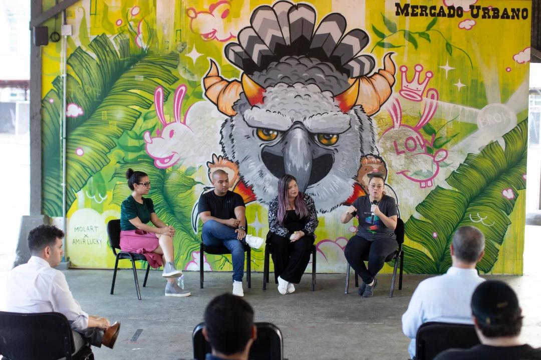 Personas reunidas escuchan las palabras de cuatro expositores